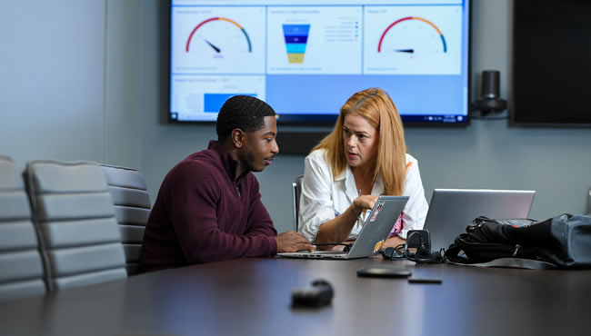 student and mentor talking while reviewing a laptop with graphs in the background